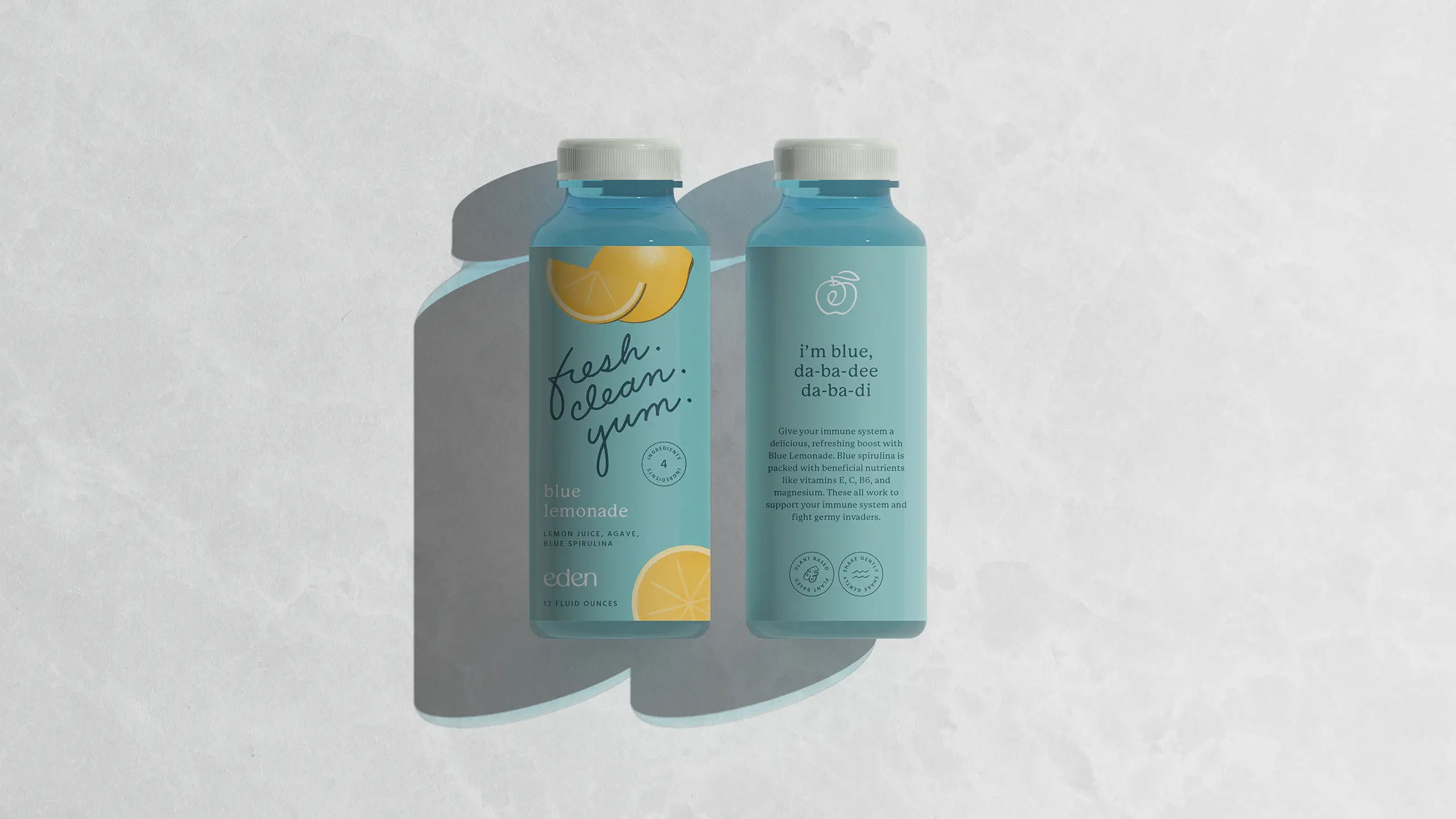 Front and back of a blue Eden lemonade bottle with lemon slice graphics and fresh. clean. yum. in script, on a light marble surface.